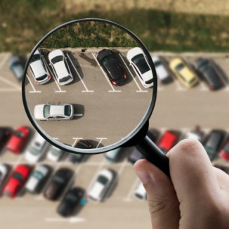 Hand holding magnifying glass over lot of cars