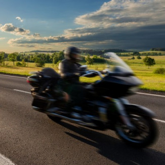 Motion-blurred black motorcycle riding on an empty asphalt road in a rural landscape at sunset